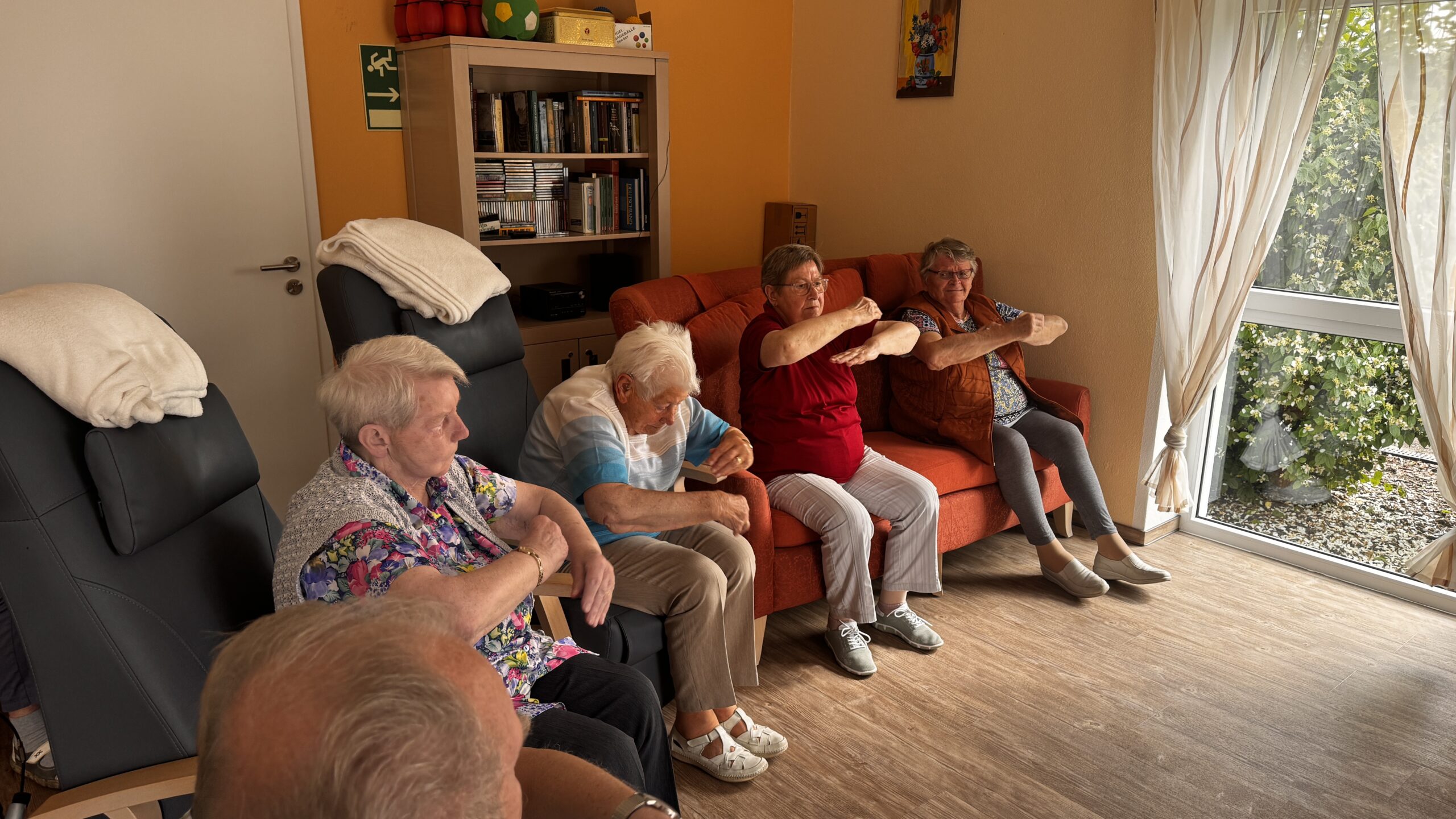 ältere Menschen sitzen zusammen und machen Sport.